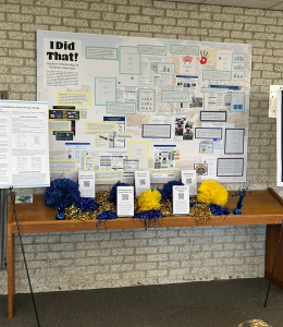 A poster sharing research is set up on a table with blue and yellow decorations