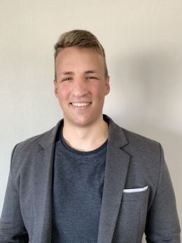 Headshot of Danny Griffin wearing a gray suit in front of a beige wall