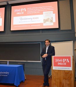 Patrick Spero leans on a podium with an "America 250 PA Delco" sign on it