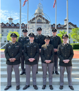 Cadets stand in uniform in front of Old Main with American flags waving in the background