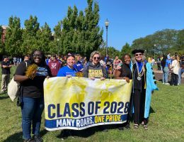 President Stacey Robertson standing outdoors behind a class of 2028 banner with four incoming students