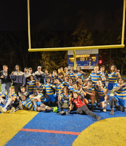 Men's rugby team pose for a photo on the field holding up their fingers to indicate number one