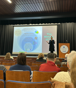 Amanda Bickerstaff stands on stage in front of a slideshow.
