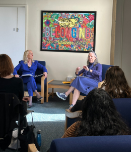 President Stacey Robertson and Rep. Mary Gay Scanlon, both wearing blue, sit in from of a colorful piece of artwork talking. 