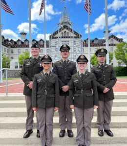 Five ROTC cadets standing in dress uniform under flags in the Bown Garden