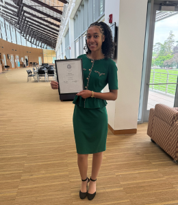 Krystal Washington, wearing a green dress, poses and smiles with an award certificate