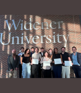 Winning students pose with their awards in front of a brown brick wall 