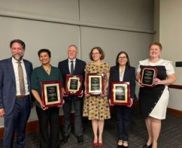 Five award winners holding their plaques, standing with the interim provost