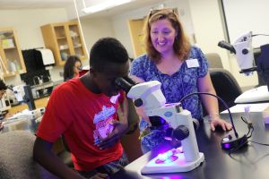 Science student looking into microscope with professor