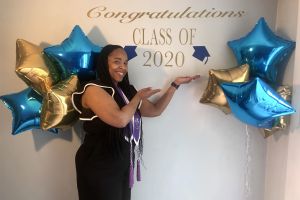 2020 Grad Student Speaker Grad student standing next to balloons and a "Congratulations Class of 2020" sign