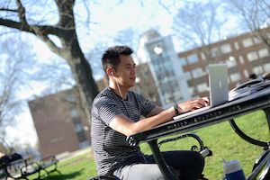 Student studying on laptop computer sitting outside at a picnic table