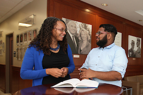 Faculty member mentoring student at table with open book