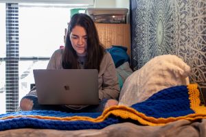 Girl in bedroom studying laptop screen