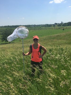 Kelsey Fisher holds a butterfly net in a grass field