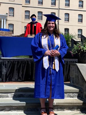 Victoria Mayer wears graduation regalia and stands on a platform