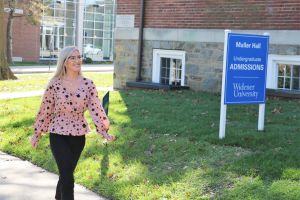 A young female student walks past Mueller Hall and a sign that reads "Admissions Office."