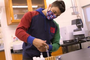 A male student in a mask conducts research in a chemistry lab.