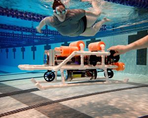 A female student swims alongside the robosub underwater to monitor the testing phase.