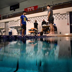 A photo half in the water captures students in the pool and on the deck testing the machine.