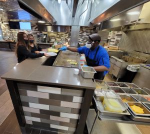 Aramark employee John Shamburger behind the grill in Pride Cafe, serving eggs to two waiting students.