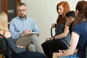 A man leads a group of young adults--three women and one man--in a drug-and-alcohol counseling session.