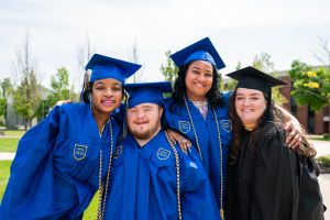 Students and a staff member pose in regalia at commencement.