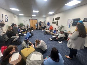 A group of people gathered in discussion, sitting on the floor and in chairs