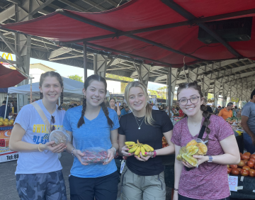 Students pose at a market with fruit 