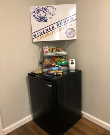 Mini fridge with snacks on top and a sign that reads "Class of 2024. Widener Bound. Congrats Kristoff"