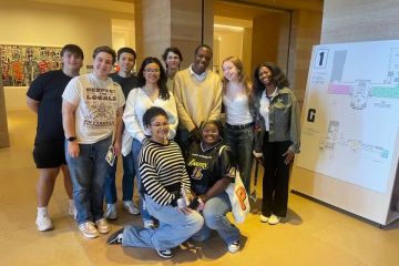 10 students huddled together in a museum smiling for the camera