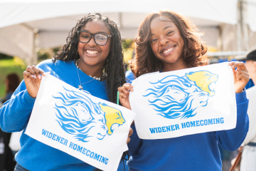 Students hold Homecoming rally towels and pose for a photo, smiling at the camera.