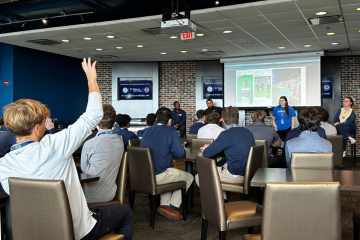 A student raises their hand with a question at a presentation.