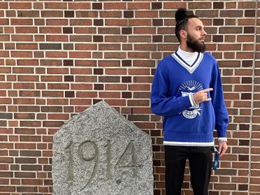 Adonijah Allsup, wearing a blue fraternity sweater, poses next to a stone marked 1914