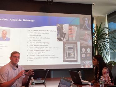 Alex Kristeller sits at a table presenting to company leaders during a summer internship.