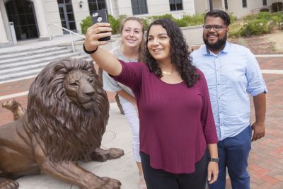students at lion statue taking selfie 