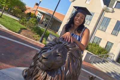 Student smiles at the Pride statue on graduation day