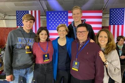 Widener students and faculty pose with Democratic primary candidate Elizabeth Warren in front of flags in New Hampshire