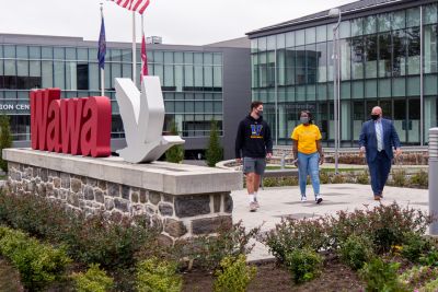 Two students and an alumnus walk together past a Wawa sign at company headquarters