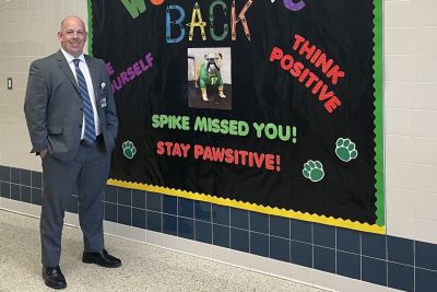 Education doctoral graduate Mike Kelly standing next to a bulletin board in a school