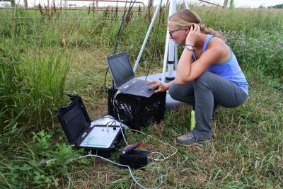 Kelsey Fisher kneels in front of a laptop in a grass field