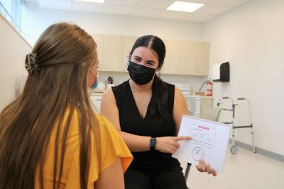 A female speech language pathology graduate student sits with a patient during a session in the clinic