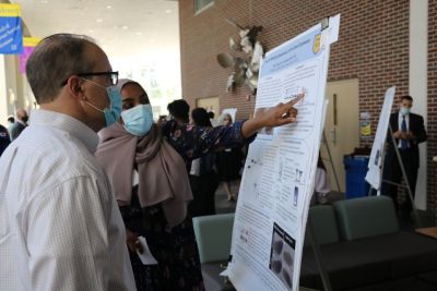 A female student engages with a guest at the SURCA Symposium while presenting their research.