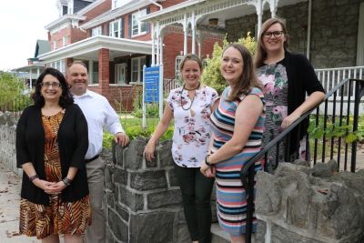 Five student success department leaders standing together outdoors in front of their buildings and a sign that says student success.