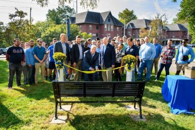 Current and alumni members of Phi Delta Theta cut a ribbon to dedicate a bench outside of the chapter house.