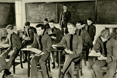 Black and white photo from 1923 of cadets at desks in a math class with their instructor in the back of the room next to the chalkboard