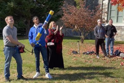 Student aims a T-shirt cannon while surrounded by faculty and staff
