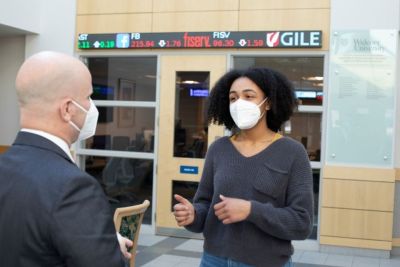 A female student engages with a business professor in front of the business lab.