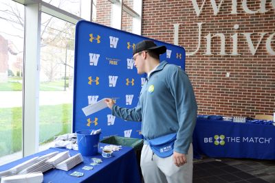 Student drops a bone marrow registry envelope into a blue bucket 