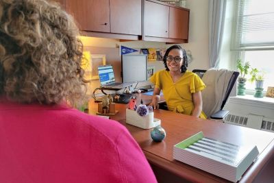 Kiara Allison seated at desk looking across in conversation with female, who is seen from behind.