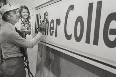 Black and white photo of President Clarence Moll painting a Widener College sign to correct the misspelling